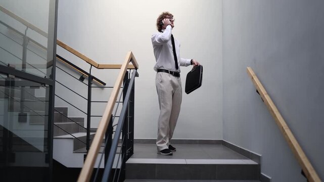 Office worker talks with colleagues on the phone while standing on the stairway with a briefcase showing teamwork business communication and the pace of a busy workday