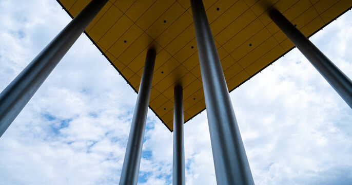 Abstract Worm's Eye View of Modern Architectural Pillars Supporting a Vibrant Yellow Canopy Against a Cloudy Blue Sky in Budapest