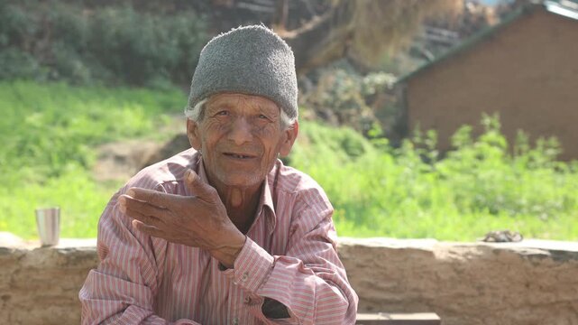 Portrait of an elderly man sitting outside his home in a rural mountain village in India, reflecting simple living, aging, and poverty in a natural countryside environment.