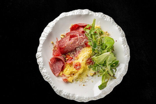 Gourmet omelet served with salami, cherry tomatoes, and a fresh green salad on a textured white plate. Dark background, professional food photography for restaurant menu and culinary concepts
