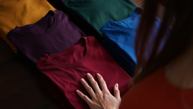 Person touching a stack of folded colorful tshirts