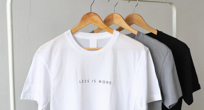 Three tshirts in white, grey, and black hanging on a clothing rack