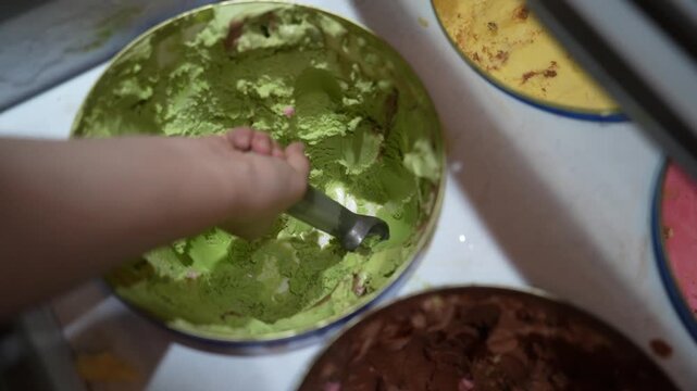 Slow motion of a woman's hand scooping pistachio ice cream