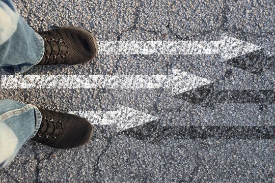 Feet on road arrows split directions choice and alternatives concept top view