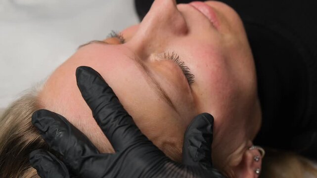 Permanent makeup master applying tint on a woman's eyebrows with a brush during a beauty treatment