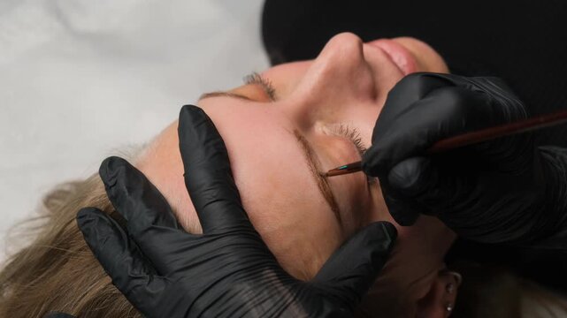 Cosmetologist performing an eyebrow tinting procedure on a client in a beauty salon