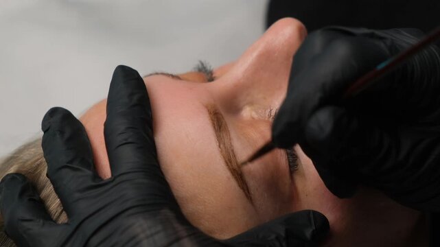 Professional artist making an eyebrow correction procedure with a brush for a young woman