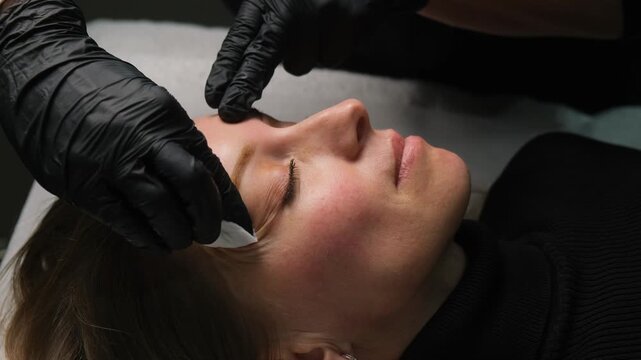 Cosmetologist preparing a client's skin for permanent makeup eyebrow tattooing in a beauty salon