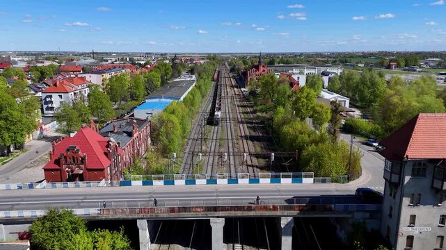High-angle aerial photograph of Nowe Skalmierzyce railway junction featuring a vintage signal box tower, a road overpass with a car, freight trains on multiple tracks, and historic red-brick buildings