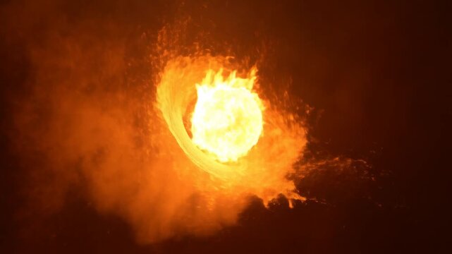 Slow motion close up tracking shot of glowing fireball swirling and ejecting sparks through smoky air in dark indoor studio environment at night