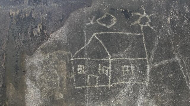 Child drawing scratched on dark dirty wall showing simple house sun tree and figure naive art street urban texture