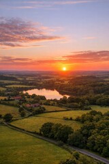 Naklejka premium Stunning sunset over serene lake. Vibrant colors fill sky and reflect on water. Peaceful landscape inspires relaxation and tranquility. Ideal image for nature lovers and travel enthusiasts.