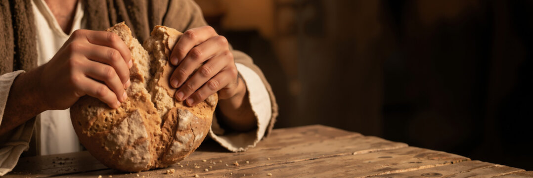 Jesus Christ breaking bread at a wooden table. Religious concept of the Last Supper. Copy space for text