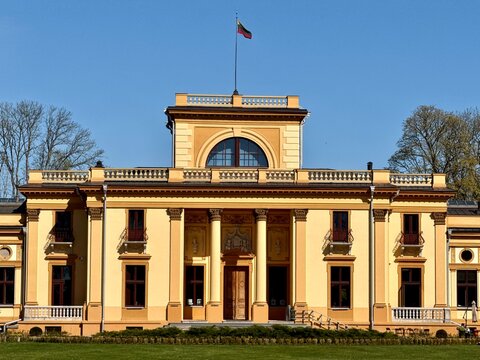 Traku Voke Manor, located in Lithuania, showcases a neoclassical architectural style with a symmetrical facade. The building features large, arched windows and columns flanking the entrance. 