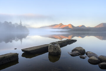 Fototapeta premium Calm reflections of mountains in lake on misty morning: Catbells and Derwentwater, Lake District, UK.