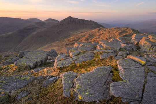 Soft evening light on rocks at sunset on a calm spring evening high up in The Lake District mountains with views of Bowfell from Crinkle Crags.