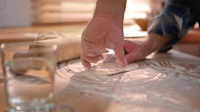 Close-up image of a chef's hand using a small glass bowl to rotate and shape the dough into cookie cutters after kneading, before baking