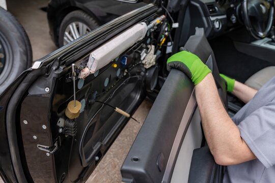 Accessing vehicle interior components. Removing door trim to access speaker and wiring system. Technician detaches door panel to facilitate speaker replacement or upgrade process