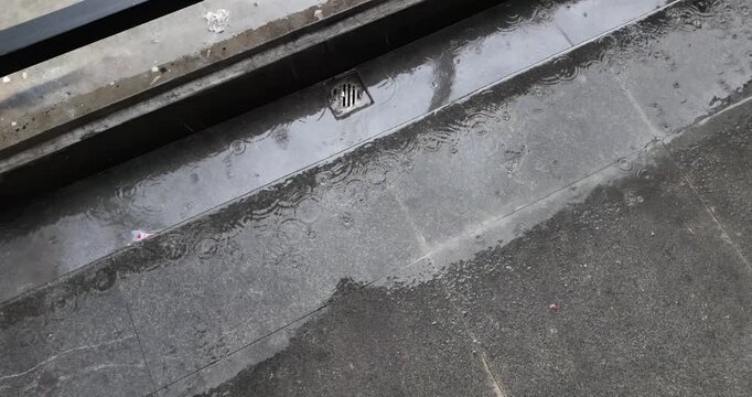 Slow motion of raindrops falling on wet stone steps, creating ripples and bubbles near a small drainage grate