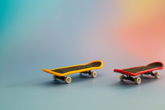 Two small toy skateboards in yellow and red stand on a smooth surface against a soft gradient background.