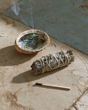 Smoking sage bundle with a shell on a natural stone surface