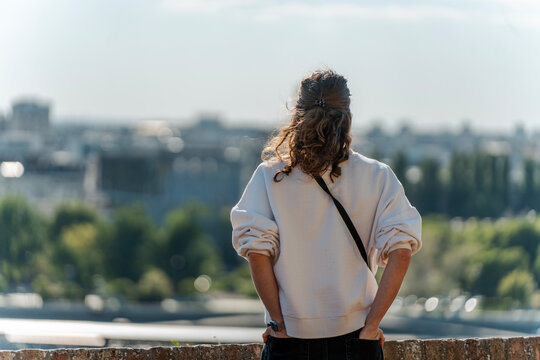 Happy young woman in white sweatshirt looking at sky and city view from above