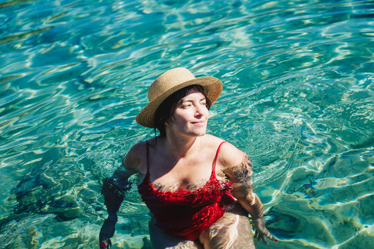 Top view of happy body positive brunette woman in red swimsuit and straw hat relaxing in turquoise sea
