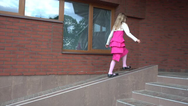 little girl in a red dress idiot on parapet near a brick building.