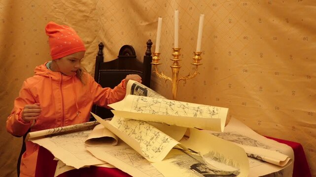 Beautiful girl in a pink jacket read old maps in knightly tent.