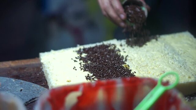 Toast seller's hand puts milk and sprinkles ceres on toast for his customer