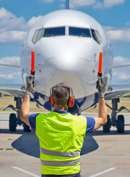 Aircraft marshaller in PPE guiding airplane on runway with marshalling wands at airport.
