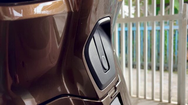 An Asian woman is closing the trunk hook located at the front of a shiny brown automatic motorcycle.