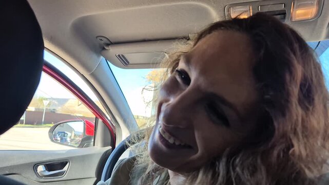 Woman driving talking, long wavy hair, having a happy conversation while commuting on a sunny day.