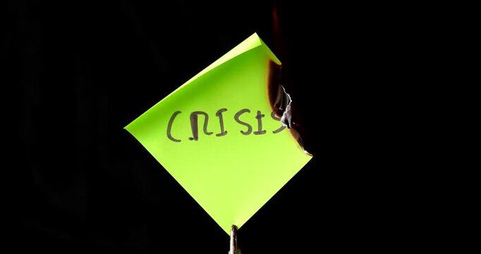 Yellow post it note with crisis text burning on black background symbolizing the end of economic problems and the start of recovery.