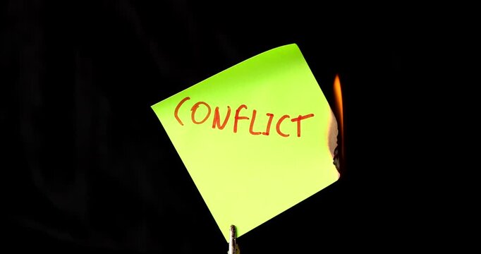 Yellow post it note with conflict text burning on black background symbolizing the end of war and the resolution of social problems.