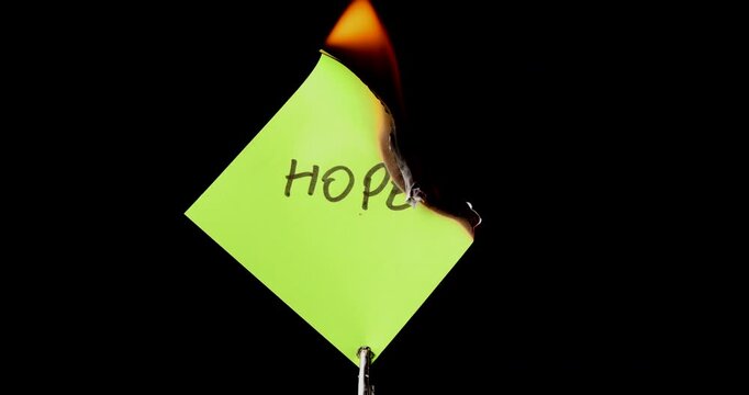 Yellow post it note with hope text burning on black background symbolizing the end of optimism and the rising feelings of despair.