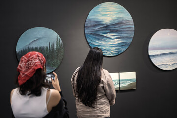 Naklejka premium Visitors admiring ocean-themed paintings at art exhibition in Delhi