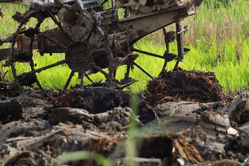 Fototapeta premium Close up of hand tractor wheel and blade plowing through wet muddy soil in rice paddy field in rural Indonesia