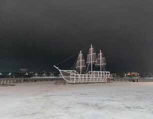 Christmas light installation of a sailing ship un a snowy night park. © Irina