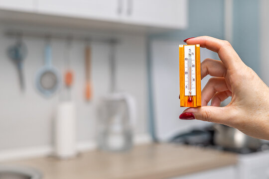 a woman's hand holding a room thermometer. hot in the kitchen. thermometer in the home kitchen. Home thermometer in degrees Celsius. room thermometer