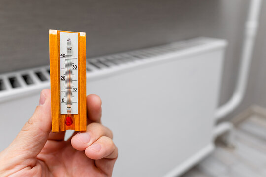 a man's hand holding a room thermometer. measuring room temperature. heat at home. heating season. high air temperature in the room. measuring the air temperature near a heating radiator
