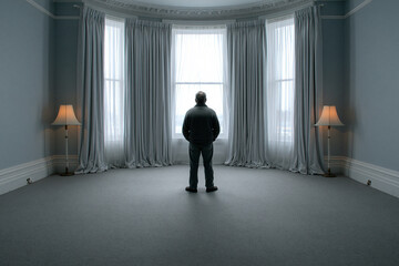 Fototapeta premium Man standing alone in empty room looking through large window