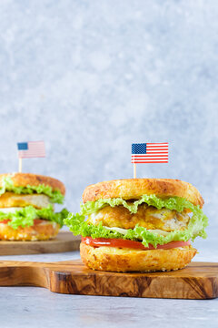 A festive bagel burger styled for Independence Day in the USA. Two bagel sandwiches on a cutting board, filled with crispy chicken, lettuce, and tomato on a gray background. space for text