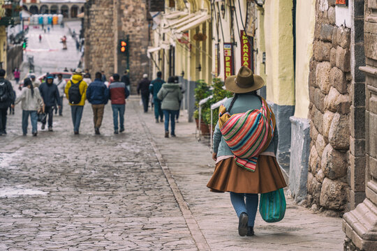 Authentic streets scene with a woman in traditional Andean dress walking down a historic cobblestone alley in Cusco