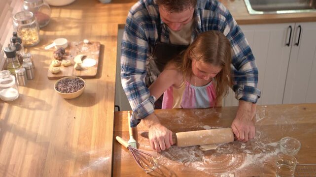 Little girl shaping dough in kitchen with father nearby, representing learning, creativity, and childhood home cooking experience