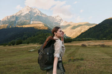 Naklejka premium A woman hiker with a large backpack stands in an open meadow, looking toward distant mountains. Bright natural light captures exploration, resilience, and hopeful wanderlust.