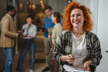 Happy red-haired woman smiling at diverse office team
