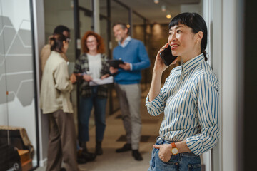 Fototapeta premium Woman talking on smart phone in office hallway with colleagues