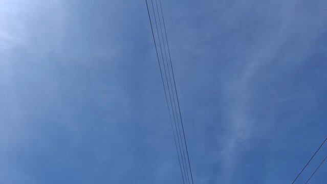 Minimalist clear blue summer sky background crossed by several thin dark parallel electrical power lines running diagonally