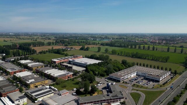 Industrial Park Aerial View: A sprawling industrial park development viewed from above, showcasing a cluster of modern warehouses and commercial buildings nestled amidst green fields and a highway.